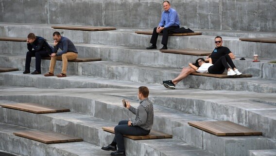 Menschen sitzen auf Holzbänken in einem Amphitheater. Menschen sitzen auf Holzbänken in einem Amphitheater. © dpa