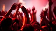 Menschen jubeln mit erhobenen Händen vor einer Bühne in rotem Licht © photocase Foto: designritter