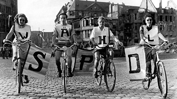 Vier Fahrradfahrer fahren mitten auf einer Straße und halten Plakate mit den Buchstaben SPD © picture-alliance / dpa 