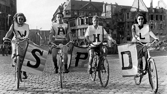Vier Fahrradfahrer fahren mitten auf einer Straße und halten Plakate mit den Buchstaben S P D © picture-alliance / dpa 