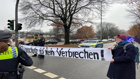 "Klimaschutz ist kein Verbrechen" steht auf einem Plakat, das von Demonstrierende über eine Straße gehalten wird © NDR Foto: Finn Kessler