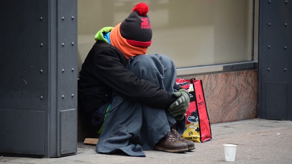 Ein warm angezogener Mann sitzt in der Innenstadt und sammelt Spenden. © dpa Foto: Daniel Bockwoldt