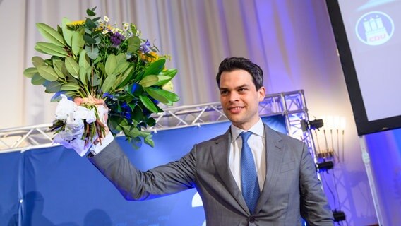 Christoph Ploß, Parteivorsitzender der CDU in Hamburg, winkt mit einem Blumenstrauß nach seiner Neuwahl zum Landesvorstand auf dem Landesparteitag der CDU Hamburg. © picture alliance/dpa Foto: Jonas Walzberg