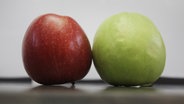 Ein roter und ein grüner Apfel liegen auf einem Tisch nebeneinander. © picture alliance / dpa Foto: Fredrik von Erichsen