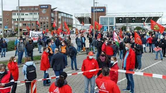 Mitarbeiter im Warnstreik stehen mit ihren Fahnen vor dem Haupteingang von Airbus in Hamburg-Finkenwerder. © picture alliance / dpa Foto: Markus Scholz