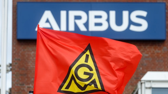 Eine Fahne der IG-Metall weht vor dem Schriftzug "Airbus" an dem Werk des Flugzeugbauers in Hamburg. © picture alliance / dpa Foto: Markus Scholz