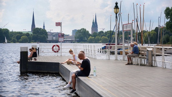 Menschen sitzen auf dem Anleger "Rabenstraße" an der Außenalster in Hamburg. © picture alliance/dpa | Jonas Walzberg 