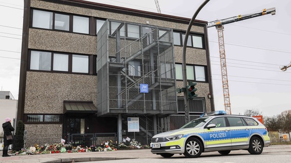 Ein Polizeifahrzeug steht auf der Straße vor dem Gemeindehaus der Zeugen Jehovas, an dem Blumen und Kerzen abgelegt wurden. © Christian Charisius/dpa Foto: Christian Charisius