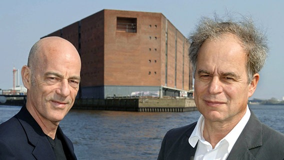 Die beiden Schweizer Architekten Jacques Herzog (l) und Pierre de Meuron in Hamburg vor dem Kaispeicher A, auf dem einmal die Elbphilharmonie stehen soll. © dpa Foto: Patrick Lux