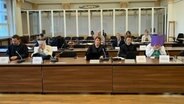 Die Angeklagten sitzen im Gerichtssaal und verdecken ihre Gesichter. © NDR Foto: Elke Spanner
