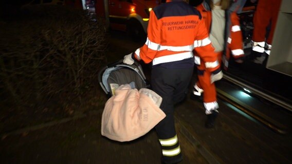 Eine Mitarbeiterin des Rettungsdienstes der Feuerwehr Hamburg trägt ein Baby in einer Babyschale zum Rettungswagen © TeleNewsNetwork Foto: Screenshot