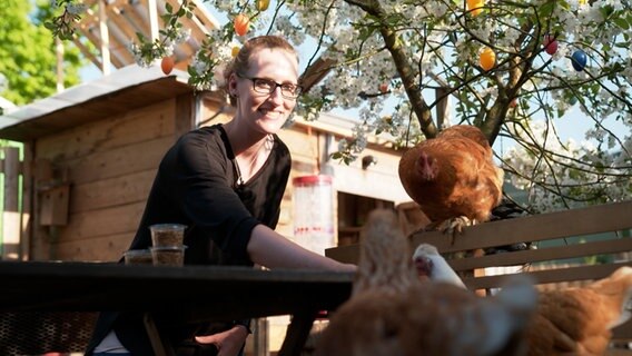 Eine junge Frau füttert Hühner. © NDR Foto: Anna Leusch