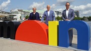 Peter Tschentscher (M, SPD), Erster Bürgermeister und Präsident des Senats der Freien und Hansestadt Hamburg, Almut Möller (SPD), Staatsrätin der Senatskanzlei, und Michael Otremba, Geschäftsführer Hamburg Tourismus GmbH, stehen vor den großen Buchstaben des Wortes "Moin" am Bootsanleger am Jungfernstieg. © picture alliance/dpa Foto: Marcus Brandt