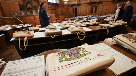 Senatsdienerinnen und Senatsdiener verteilen Stoffbeutel und Informationen auf den Tischen im Plenarsaal der Hamburgischen Bürgerschaft. © dpa Foto: Christian Charisius