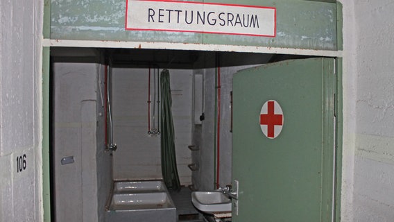 Durch eine Tür mit einem roten Kreuz geht der Blick im Bunker in der Hamburger Methfesselstraße in einen Raum mit Duschen. © NDR Foto: Daniel Sprenger