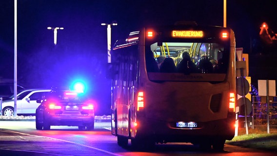 Ein Polizeiauto mit eingeschaltetem Blaulicht eskortiert einen Bus voll Menschen auf dem "Evakuierung" steht am Flughafen. Der Hamburger Flughafen ist nach dem Eindringen eines Fahrzeugs auf das Gelände gesperrt worden. © picture alliance / dpa Foto: Jonas Walzberg