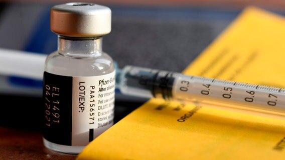 Eine Dose Impfstoff von Biontech/Pfizer, eine Spritze und ein gelber Impfpass liegen auf einem Tisch. © picture alliance / Laci Perenyi 