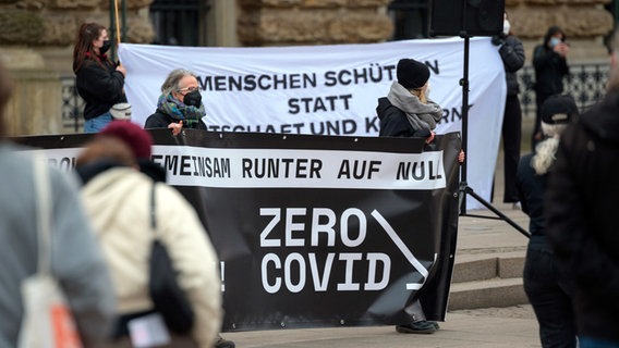 Kurz vor dem Inkrafttreten der Ausgangsbeschränkungen in Hamburg zeigen Demonstranten Plakate mit der Aufschrift "Gemeinsam runter auf Null - Zero Covid". © dpa Foto: Jonas Walzberg/dpa