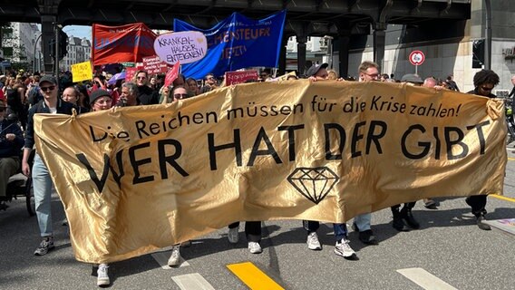 "Die Reichen müssen für die Krise zahlen! Wer hat der gibt" steht auf einem Transparent, hinter dem sich Demonstranten im Hamburger Stadtteil Eppendorf am 1. Mai 2023 versammelt haben. © NDR Foto: Ingmar Schmidt