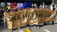 "Die Reichen müssen für die Krise zahlen! Wer hat der gibt" steht auf einem Transparent, hinter dem sich Demonstranten im Hamburger Stadtteil Eppendorf am 1. Mai 2023 versammelt haben. © NDR Foto: Ingmar Schmidt