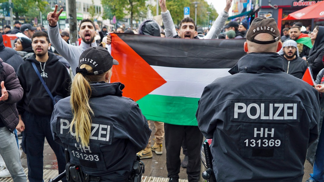 Polizisten stehen in Hamburg am Steindamm vor Demonstranten, die eine palästinensische Flagge halten.
