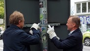 Jens Kerstan (Grüne), Umweltsenator, und Andy Grote (SPD), Innensentor, schrauben gemeinsam ein Straßenschild ab. © NDR 