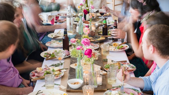 Menschen sitzen an einem Tisch mit Essen und unterhalten sich. (Symbolbild) © picture alliance / Bildagentur-online/Tetra Images 