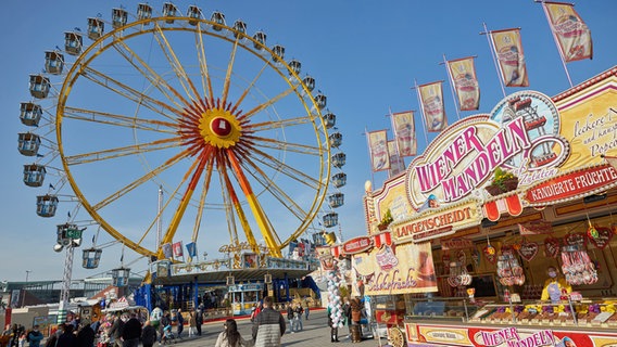 Besucher gehen über den Hamburger Dom auf dem Heiligengeistfeld. Im Hintergrund ist ein Riesenrad zu sehen. © picture alliance / dpa Foto: Georg Wendt