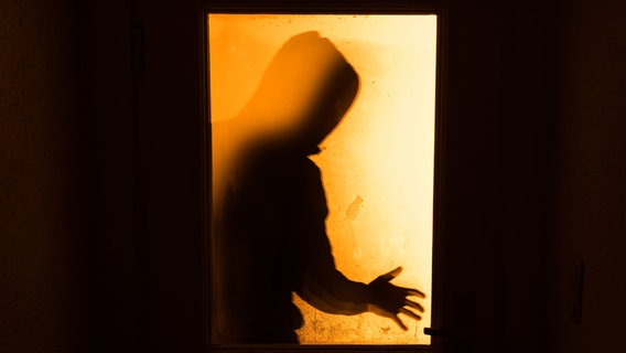 Der Schatten eines Mannes ist hinter einer gläsernen Wohnungstür zu sehen. © dpa Foto: Nicolas Armer
