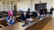 Im Prozess um einen Einbruch in der Hafencity sitzen zwei Angeklagte im Gerichtssaal und verdecken ihre Gesichter. © NDR Foto: Elke Spanner