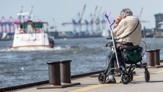 Eine alte Frau sitzt an der Elbe auf den Landungsbrücken auf ihrem Rollator. © dpa Foto: Markus Scholz