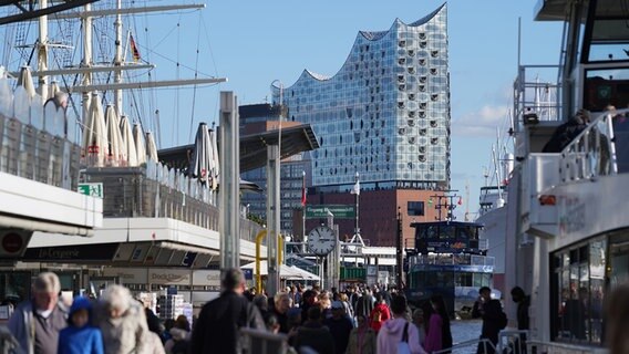 Passanten genießen das sonnige Wetter an den Landungsbrücken im Hamburger Hafen. im Hintergrund ist die Elbphilharmonie zu sehen. © picture alliance/dpa | Marcus Brandt Foto: Marcus Brandt