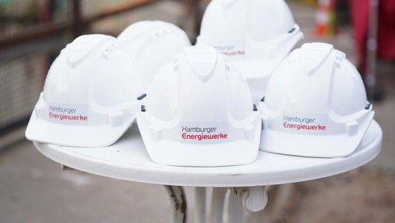 Bauarbeiterhelme mit dem Schriftzug "Hamburger Energiewerke" liegen auf einem Tisch. © picture alliance/dpa Foto: Marcus Brandt