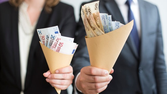 Symbolbild zum Thema Equal Pay Day: Eine Frau und ein Mann halten unterschiedlich große Papiertüten gefüllt mit Geldscheinen in den Händen. © picture alliance / photothek 