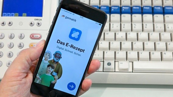 Eine App, die das E-Rezept anzeigen kann, wird in einer Apotheke vor einem Lesegerät und einer Tastatur gezeigt. © picture alliance/dpa Foto: Jens Kalaene