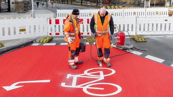 Arbeiter tragen auf einer neu eingerichteten Fahrradspur auf der Esplanade in Hamburg ein Fahrrad-Logo auf. © dpa Foto: Markus Scholz