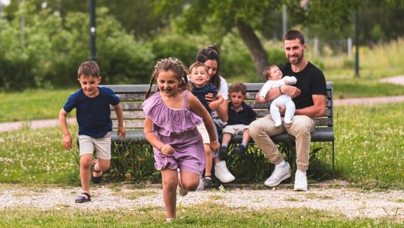 Eine Familie sitzt auf einer Parkbank im Grünen. © picture alliance Foto:  Josu Acosta