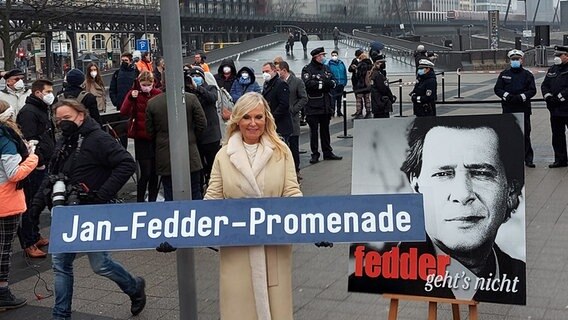 Eine Frau hält ein Straßenschild, auf dem "Jan-Fedder-Promenade" steht © NDR / Karsten Sekund Foto: Karsten Sekund