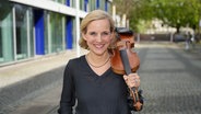 Angelika Bachmann schultert ihre Geige und steht strahelnd auf dem NDR-Gelände am Rothenbaum. © NDR Foto: Marco Peter