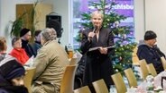 Hamburgs Bischöfin Kirsten Fehrs liest in der Tagesaufenthaltsstätte für Wohnungslose der Diakonie die Weihnachtsgeschichte und singt mit den Besuchern Weihnachtslieder. © picture alliance/dpa | Markus Scholz Foto: picture alliance/dpa | Markus Scholz