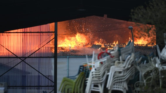 Flammen steigen bei einem Großbrand in Hamburg-Rothenburgsort aus einer Lagerhalle, im Vordergrund ist Schrott gestapelt. © Jonas Walzberg/dpa 