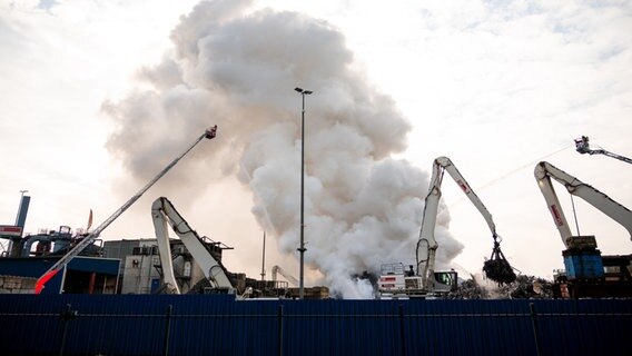 Feuerwehrleute löschen einen brennenden Schrotthaufen im Harburger Hafen. © Daniel Bockwoldt/dpa 
