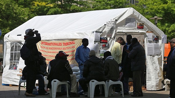 Afrikanische Flüchtlinge stehen vor einem Informationszelt nahe des Hauptbahnhofes in Hamburg. © dpa Foto: Christian Charisius