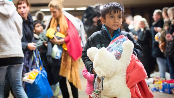 Ein Flüchtlingsjunge steht mit Geschenken in den Armen im Bahnhof in Hamburg-Harburg. © dpa Foto: Daniel Reinhardt