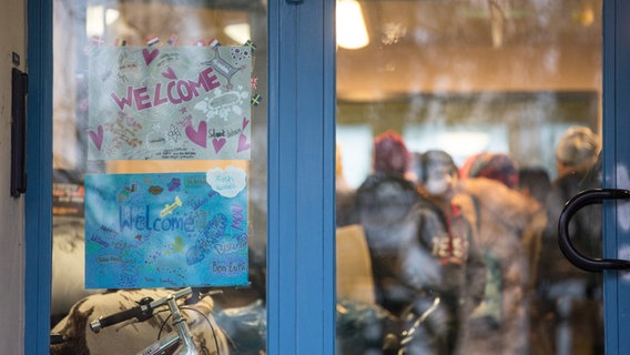 Flüchtlinge in Hamburg hinter eine Glastür auf der Willkommen steht © Picture Alliance / Christian Charisius Foto: / Christian Charisius