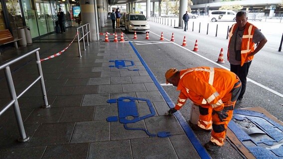 Arbeiter malen am Hamburger Flughafen Parkplatzmarkierungen für E-Taxis auf den Boden.  
