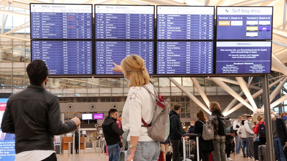 Reisende schauen am Flughafen Hamburg auf eine Anzeigetafel. © picture alliance / dpa Foto: Bodo Marks