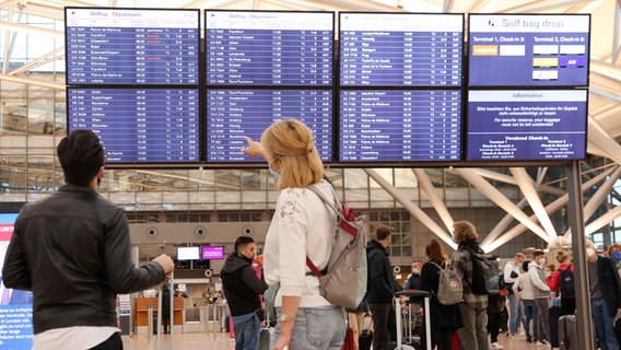 Reisende schauen am Flughafen Hamburg auf eine Anzeigetafel. © picture alliance / dpa Foto: Bodo Marks