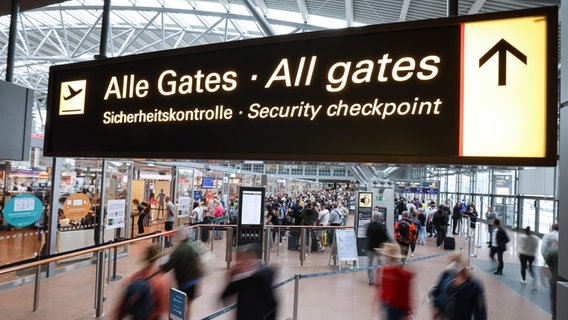 Flugreisende sind am Eingang zu den Sicherheitskontrollen am Airport Hamburg unterwegs. © picture alliance/dpa Foto: Christian Charisius