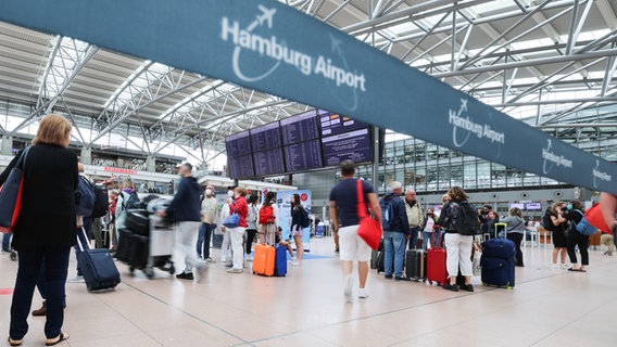 Flugreisende stehen unter den Anzeigetafeln und vor den Check-In Schaltern in Terminal 1 am Airport Hamburg. © picture alliance/dpa Foto: Christian Charisius